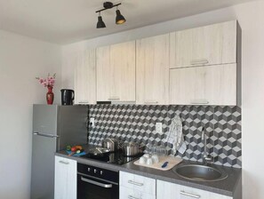 A modern kitchen with light wood cabinets, a black and white patterned backsplash, stainless steel appliances, and a countertop with cooking utensils.