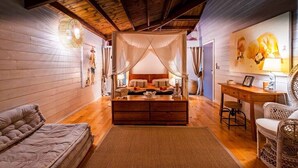 Una camera da letto accogliente con soffitto in legno, un letto a baldacchino, una scrivania in legno, poltrone in vimini e una lampada a parete.
