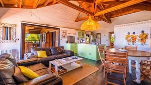 Un'ampia zona giorno con divano in pelle, un tavolo da pranzo con sedie, angolo cottura e un grande soffitto in legno.