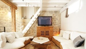 A cozy living room with a stone wall, a wooden TV stand, and wicker sofas. - L'ESTAOU DE FINOU*** (Saint-Paul-et-Valmalle)