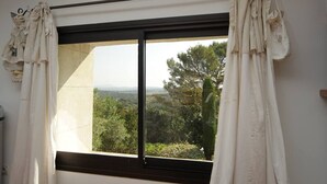 A window with white curtains, a black frame, and a view of greenery and trees outside. - L'ESTAOU DE FINOU*** (Saint-Paul-et-Valmalle)