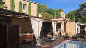 Une terrasse en bois avec un jacuzzi, des sièges d’extérieur et un bâtiment en pierre doté d’un patio couvert.