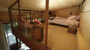 Ein Schlafzimmer in einer Holzhütte mit einer Glaswand, einem Bett, einem Sessel und einem hängenden Traumfänger.