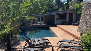 Eine Holzterrasse mit Pool, Liegestühlen und einer überdachten Veranda.