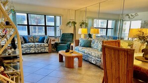 Un salon avec un canapé, un fauteuil et une table basse. On y trouve également une bibliothèque et un miroir accroché au mur.