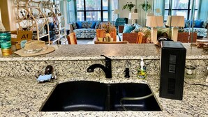 Une cuisine dotée de plans de travail en granit, d’un évier noir et d’un coin repas avec un canapé bleu et des chaises en osier.