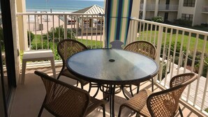 Un balcon doté d’une table ronde et de chaises en osier, offrant une vue sur une plage et un immeuble avec des balcons.