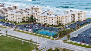 A beachfront hotel with multiple buildings, a parking lot, and a tennis court.