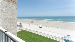 Blick auf einen Strand von einem Balkon aus, mit einer Rasenfläche und einem Zaun.