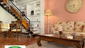 Un salon avec un escalier, un canapé, une table basse et une horloge au mur.