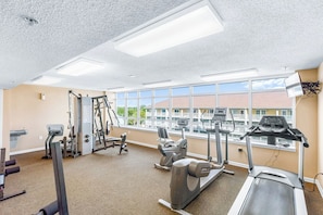 A gym with cardio machines, weight equipment, and large windows offering a view of buildings.