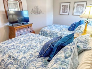 Una habitació d'hotel amb dos llits, una televisió sobre un moble de fusta i una obra d'art a la paret.
