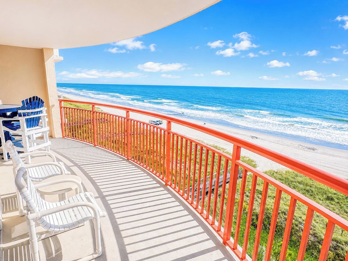 A balcony with a view of the ocean, featuring a railing and several chairs.