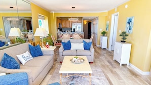 A living room with a grey sofa, blue cushions, a coffee table, and a dining area with a table and chairs.