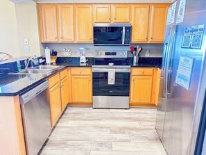 Una cocina con armarios de madera, microondas, horno, lavavajillas y refrigerador.