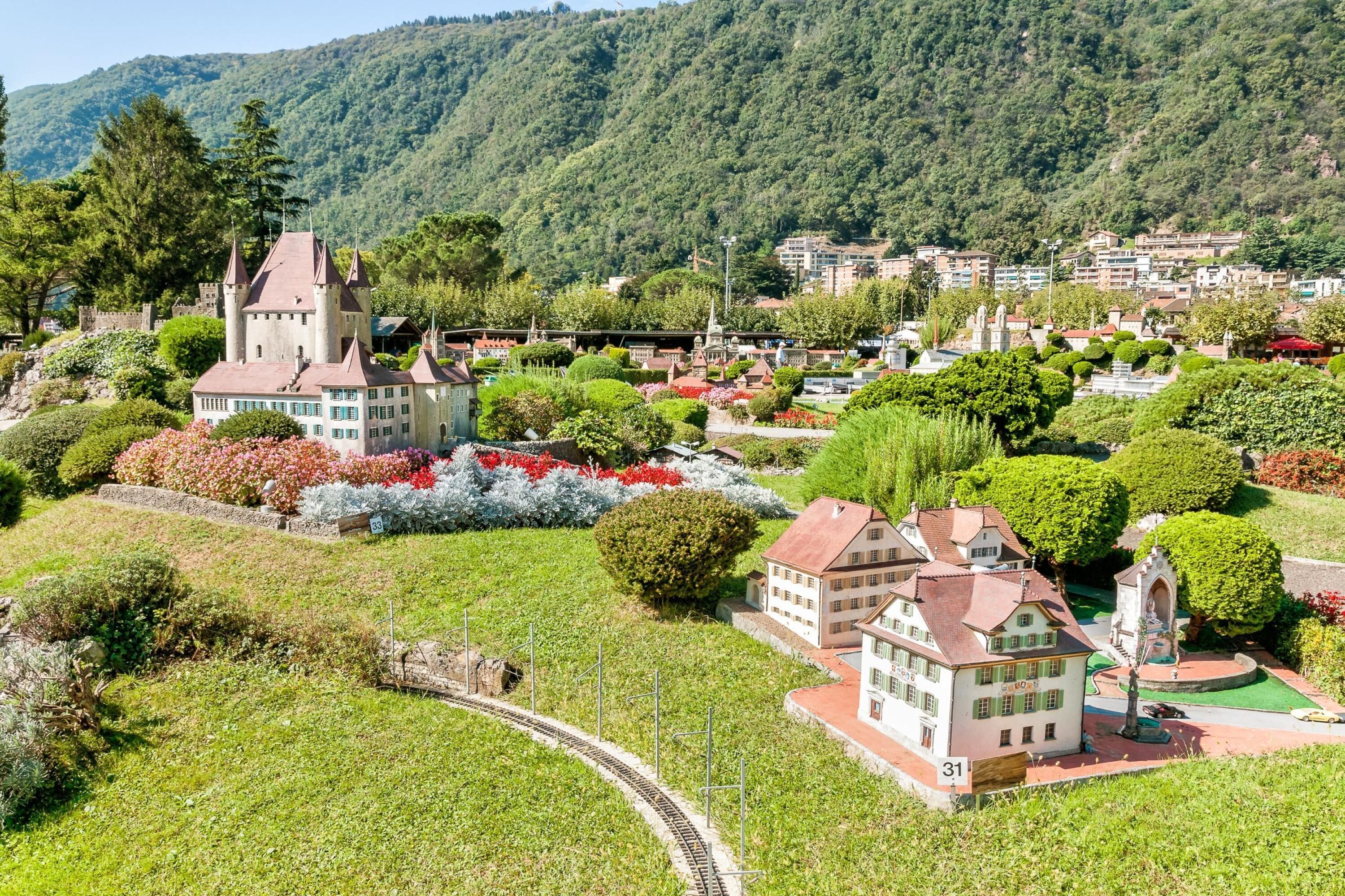 Un réseau de trains miniatures comprenant un château, une église et des immeubles résidentiels, le tout intégré dans un paysage verdoyant et vallonné.