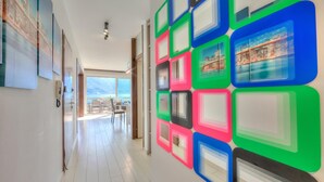 Passadís amb quadres de formes quadrades i colors a la paret, vista de la zona de menjador i una porta que dona a un balcó.