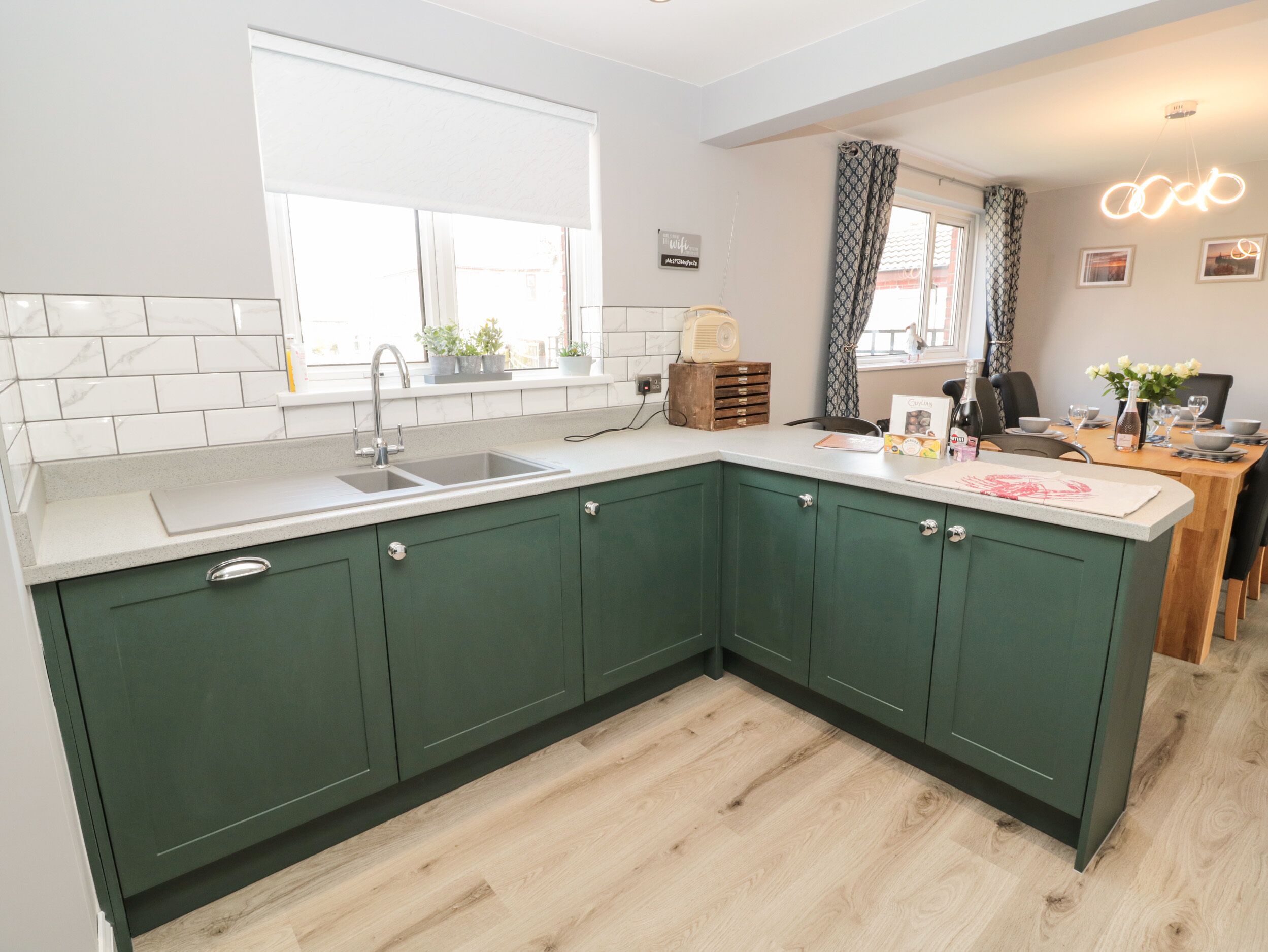 A kitchen with green cabinets, a white countertop, and a window with blinds.