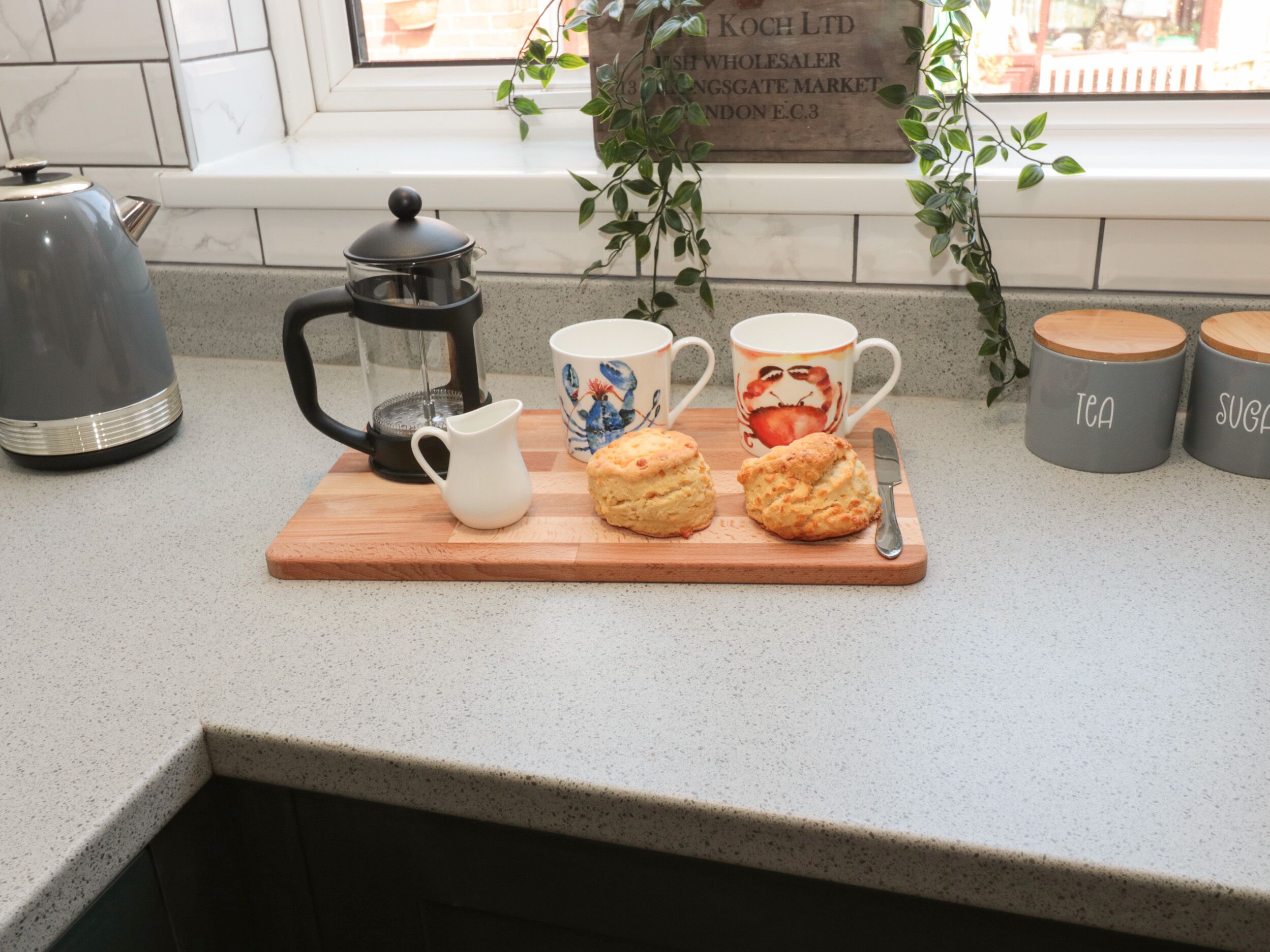 A kitchen counter with a coffee maker, a white pitcher, two scones, and a knife.
