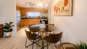 A modern kitchen with wooden cabinets, a stainless steel refrigerator, a dining table with four chairs, and a chandelier. - Charming 2 BR riverside stopover in Gold Hill. Private hot tub, river access, and just down the road from Del Rio Vineyards. Perfect base for exploring the Rogue Valley. Pet-friendly! (Gold Hill)