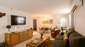 A modern living room with a flat-screen TV, a wooden coffee table, a brown sofa, and a dining area with chairs and a table. - Charming 2 BR riverside stopover in Gold Hill. Private hot tub, river access, and just down the road from Del Rio Vineyards. Perfect base for exploring the Rogue Valley. Pet-friendly! (Gold Hill)