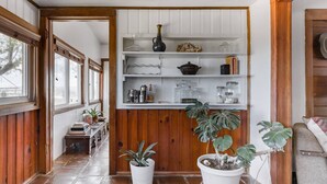 Un pasillo con paneles de madera, un estante blanco con diversos objetos y plantas en macetas.