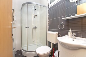 Un baño moderno con ducha envuelta en vidrio, inodoro blanco y lavamanos con dispensador de jabón.