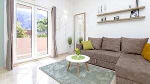 Ein Wohnzimmer mit einer braunen Couch, einem kleinen weißen Tisch und Bergblick durch eine Schiebetür.