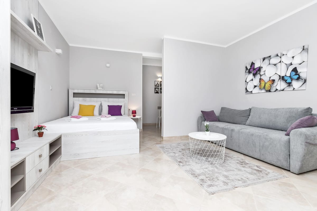 Un dormitorio moderno con una cama, un sofá gris, un televisor y una obra de arte en la pared.