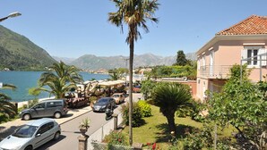 Ein Hotel an der Küste mit Blick auf das Meer und die Berge. Im Vordergrund sind geparkte Autos und eine Palme zu sehen.
