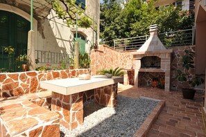 Un patio al aire libre con una mesa y asientos de piedra, una chimenea de piedra y una zona con grava.