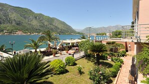 Eine Küstenansicht mit einem Gebäude, einer Terrasse mit Sonnenschirmen und einem Berg im Hintergrund.