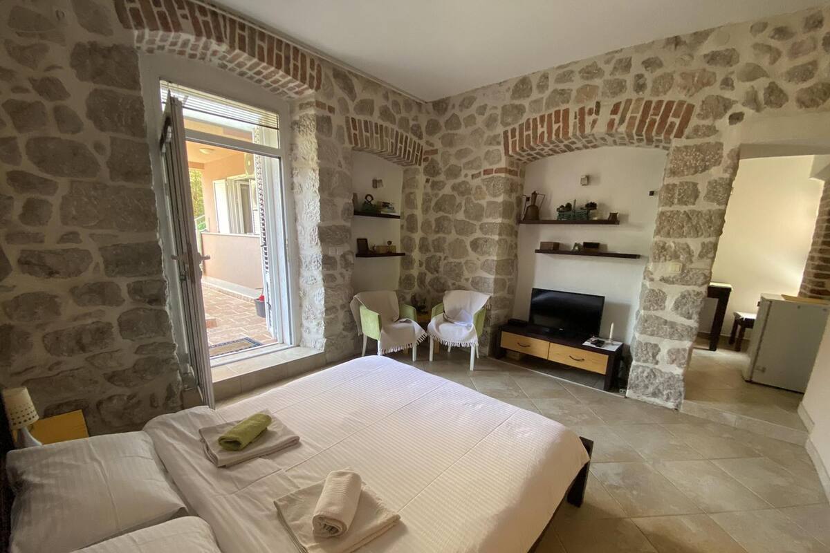 Un dormitorio con paredes de piedra, una cama con ropa blanca, un televisor, una silla y una mesita.