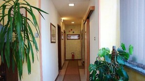 A narrow hallway with a fire extinguisher, framed pictures on the walls, and potted plants. - HOTEL LA PERGOLETTA (Orvieto)