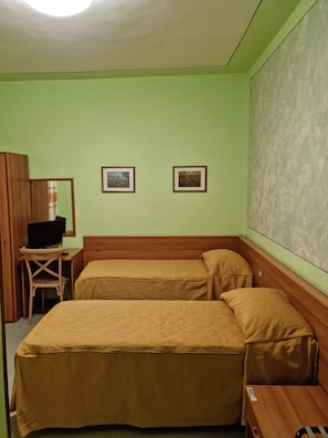 A room with two beds, a desk with a computer, and two framed pictures on the wall.