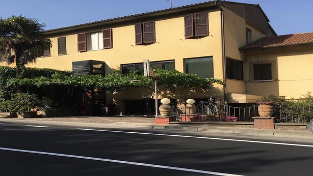 A two-story building with a yellow facade, multiple windows with brown shutters, and a visible entrance with a canopy. - HOTEL LA PERGOLETTA (Orvieto)
