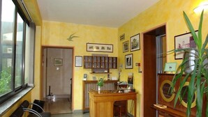 A room with a wooden desk, chairs, a radiator, framed pictures on the wall, and a window with a view. - HOTEL LA PERGOLETTA (Orvieto)