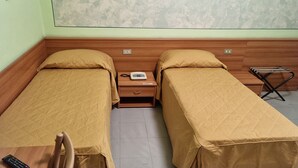 A room with two single beds, a nightstand with a lamp, a small table, and a window with a view of a mountainous landscape. - HOTEL LA PERGOLETTA (Orvieto)