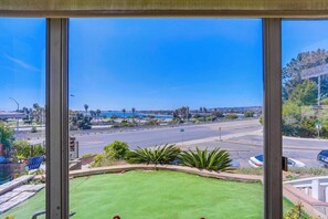 A view from a window overlooking a green lawn, a road, and a body of water.