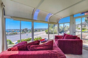 A room with a large window offering a view of a road and greenery. There is a red sofa with cushions. - View of Mission Bay plus A/C, pets, and parking (San Diego)