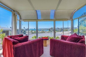 A room with a large window offering a view of a road and greenery. There are two red upholstered chairs and a small table with a plant. - View of Mission Bay plus A/C, pets, and parking (San Diego)