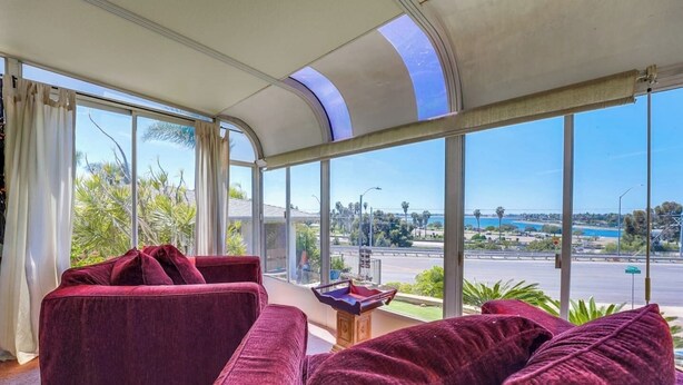 A modern living room with a curved ceiling and large windows offering a view of a cityscape and water. - View of Mission Bay plus A/C, pets, and parking (San Diego)