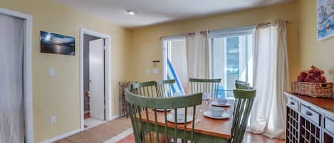 Un comedor con una mesa dispuesta para cuatro personas, sillas, una ventana con cortinas y vistas al exterior.
