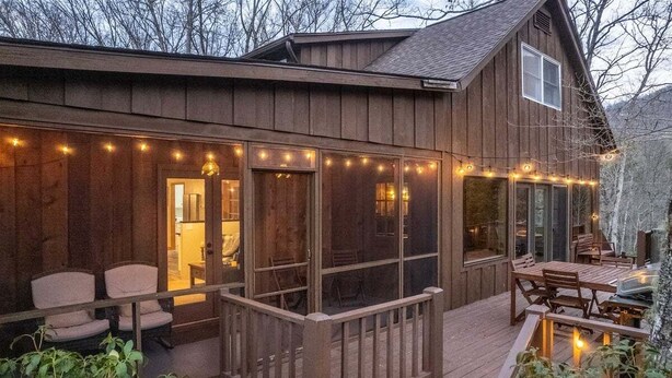 Una cabaña de madera con un porche cubierto, ventanas amplias y luces colgantes.