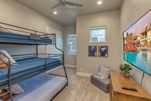 Una habitación con literas, televisión, control remoto y ventana con vista a una casa.