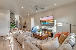 A spacious living room with a large flat-screen TV mounted on the wall, a comfortable sectional sofa, a wooden coffee table, and a staircase leading to another level.
