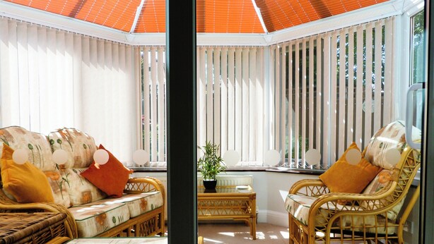 Een zonnige kamer met rieten meubels, een klein tafeltje en een plant in pot.
