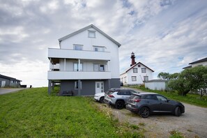 A two-story building with a flat roof and a small balcony. There are two cars parked in front.