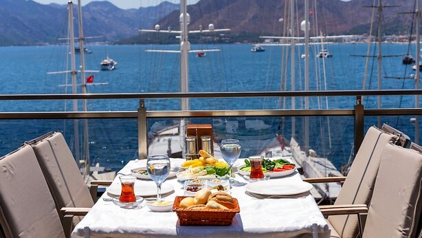 A table set for a meal with a view of sailboats and mountains in the background. - Liman Deluxe Hotel (Marmaris)