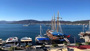 A marina with various boats docked, including a large ship and smaller yachts, with a clear view of the water and distant hills. - Liman Deluxe Hotel (Marmaris)